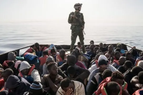 Man in military uniform on a boat with migrants